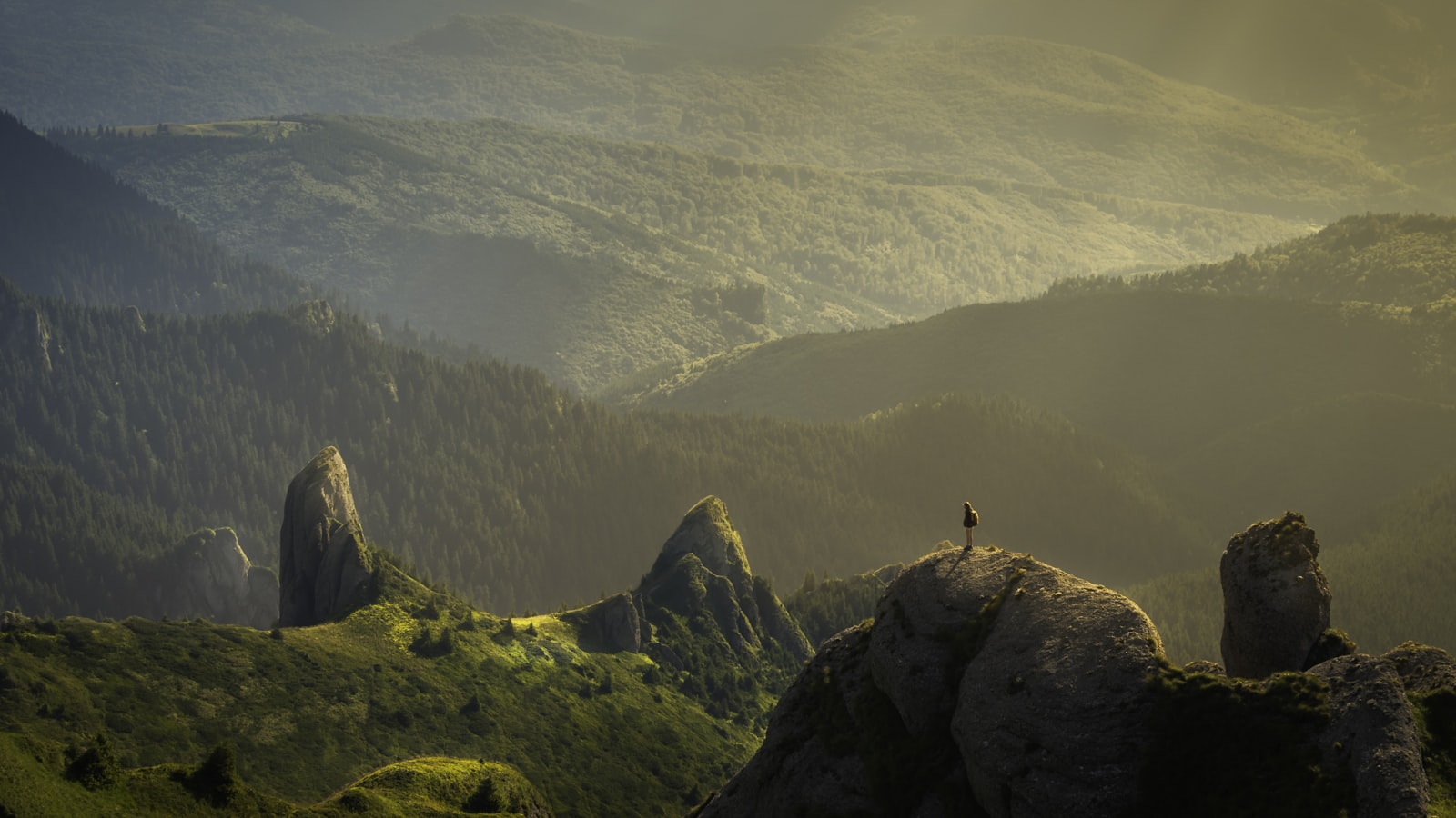 A traveler standing on a ridge at golden hour, looking out over a wide valley.